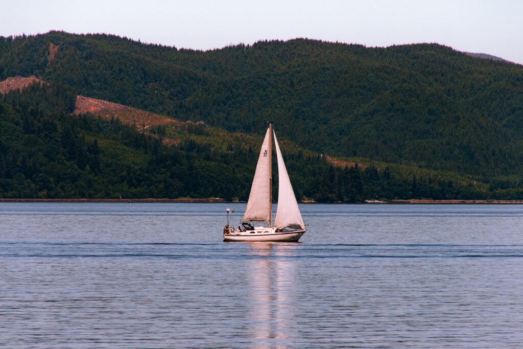 sailboat sailing in a beautiful river with a forest on a steep hill in the background